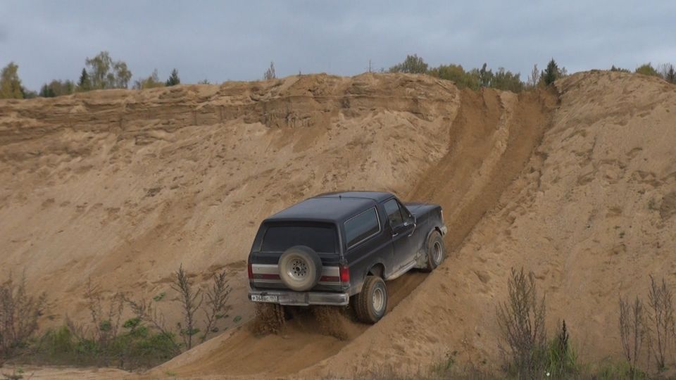 Black Ford Bronco driving up a sand dune.