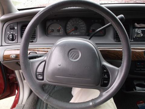 1999 Mercury Grand Marquis - The interior of a 1999 Mercury Grand Marquis shows the steering wheel with cruise control buttons and the dashboard with gauges. The wood g…