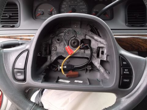 1999 Mercury Grand Marquis - The interior of a car shows a steering wheel with the airbag removed, revealing wiring and components underneath. Visible buttons on the st…