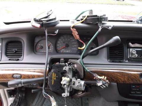 1999 Mercury Grand Marquis - The interior of a 1999 Mercury Grand Marquis shows a disassembled steering column with wiring harnesses and components exposed. The dashboa…