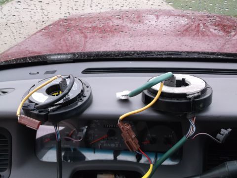 1999 Mercury Grand Marquis - Two clock spring assemblies are shown resting on the dashboard of a vehicle. Wires and connectors are visible, along with a portion of the…