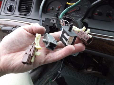 1999 Mercury Grand Marquis - A person's hand holds several electrical connectors and switches removed from a vehicle's steering column. The dashboard and instrument clu…