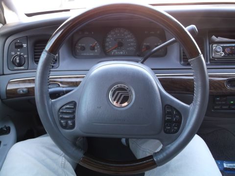 1999 Mercury Grand Marquis - The interior of a 1999 Mercury Grand Marquis is shown, focusing on the steering wheel and dashboard. The steering wheel has wood trim and c…