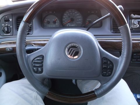 1999 Mercury Grand Marquis - The interior of a 1999 Mercury Grand Marquis shows a close-up of the steering wheel with cruise control buttons and the dashboard gauges. T…