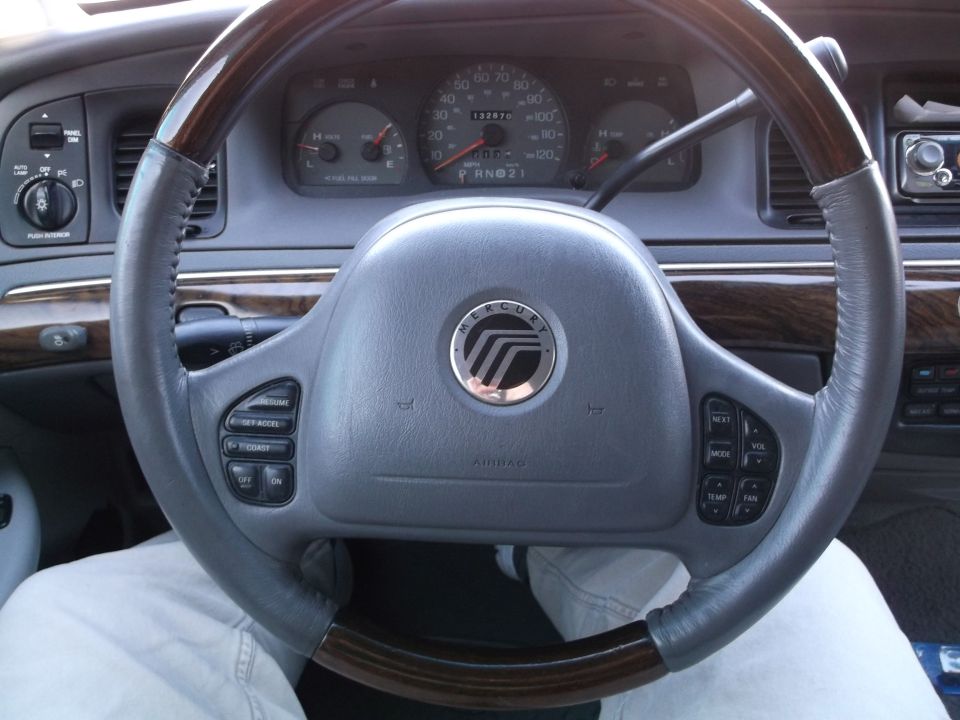 Interior of a 1999 Mercury Grand Marquis showing steering wheel, dashboard gauges, and wood trim.
