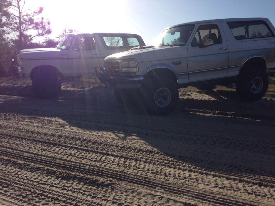 Two lifted Ford Broncos on a sandy surface.
