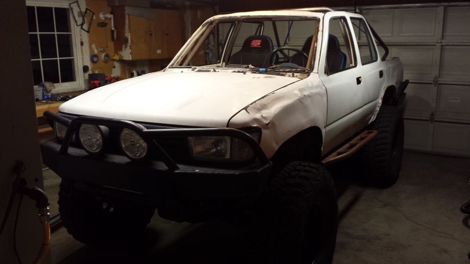 White Toyota 4Runner with roll cage and off-road mods in a garage.