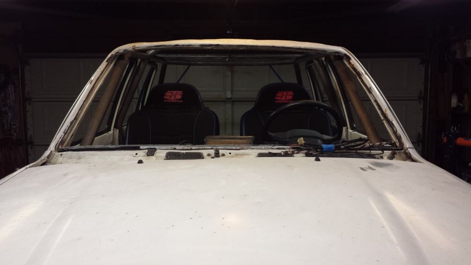 Interior front view of a white vehicle with roll cage, racing seats, and steering wheel.
