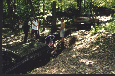 1991 Ford Bronco - Off-roaders attempt to free two vehicles stuck in a muddy ditch in a wooded area.