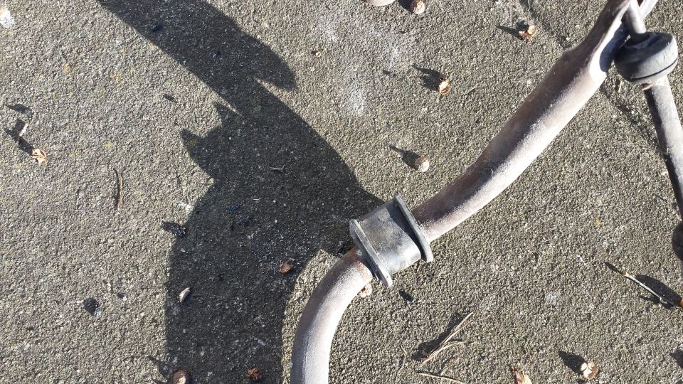 Rusty metal sway bar with black rubber bushing on concrete