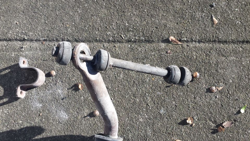Car sway bar end link with bushings and bracket on concrete.