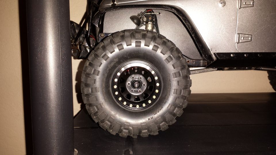 RC rock crawler Jeep Wrangler front wheel and fender, grey body, aggressive off-road tire.