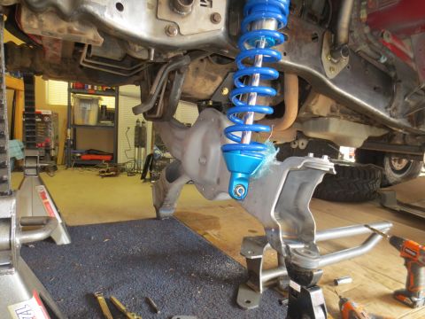 1996 Ford Bronco - A blue coilover shock absorber is installed on the underside of a vehicle, likely a 1996 Ford Bronco, in a garage setting. The vehicle is s…