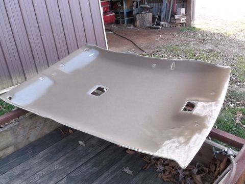1999 Mercury Grand Marquis - A tan headliner for a 1999 Mercury Grand Marquis is laid out on a wooden surface, possibly a trailer. The headliner has cutouts for interio…