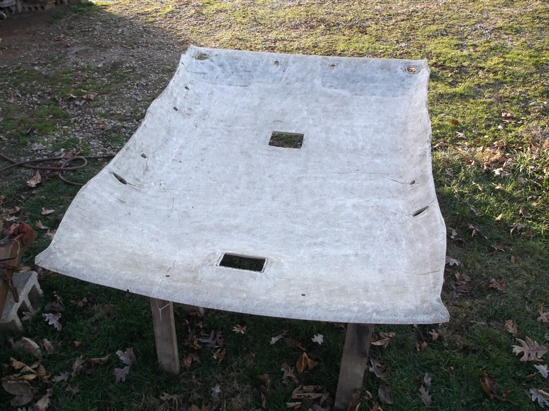 Detached car headliner with cutouts, laid out on wooden supports outdoors.