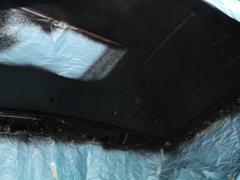 1999 Mercury Grand Marquis - The underside of a vehicle's roof is being spray painted black. Blue tarps are used to protect the surrounding area from overspray.