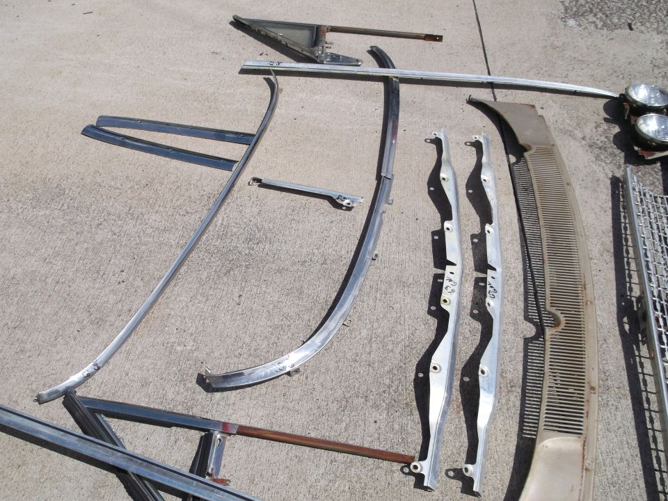 Automotive trim pieces including headlights, grilles, and chrome strips on concrete.