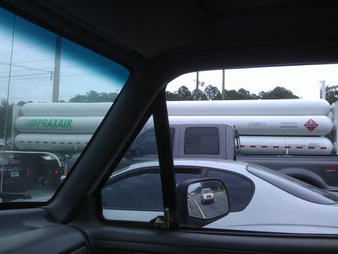 1994 Ford Bronco - View from inside a vehicle looking out at a truck carrying large white hydrogen compressed tanks. A white car is in the foreground, and a b…