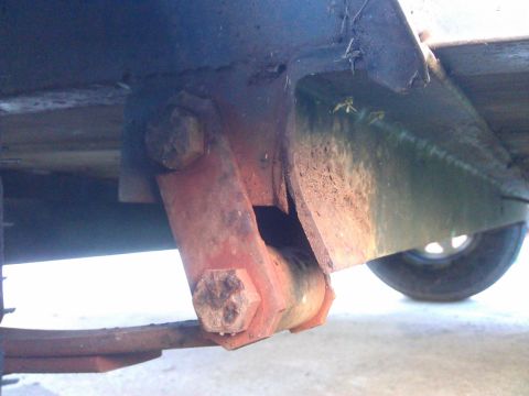 1994 Ford Bronco - A close-up view of the rusted suspension components on the underside of a vehicle, including a leaf spring, shackle, and bolt. The scene is…