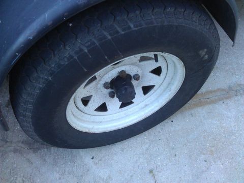 1994 Ford Bronco - A close-up view of a worn tire and white rim on a trailer or vehicle. The tire shows significant tread wear and some cracking, with a black…