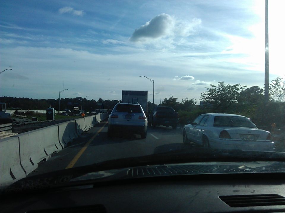Rear view of a light-colored sedan in traffic on a highway construction zone.