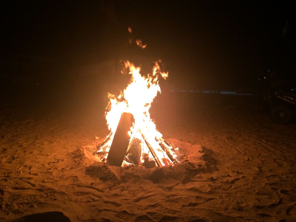 Bonfire on a beach at night with a vehicle silhouette in the background.