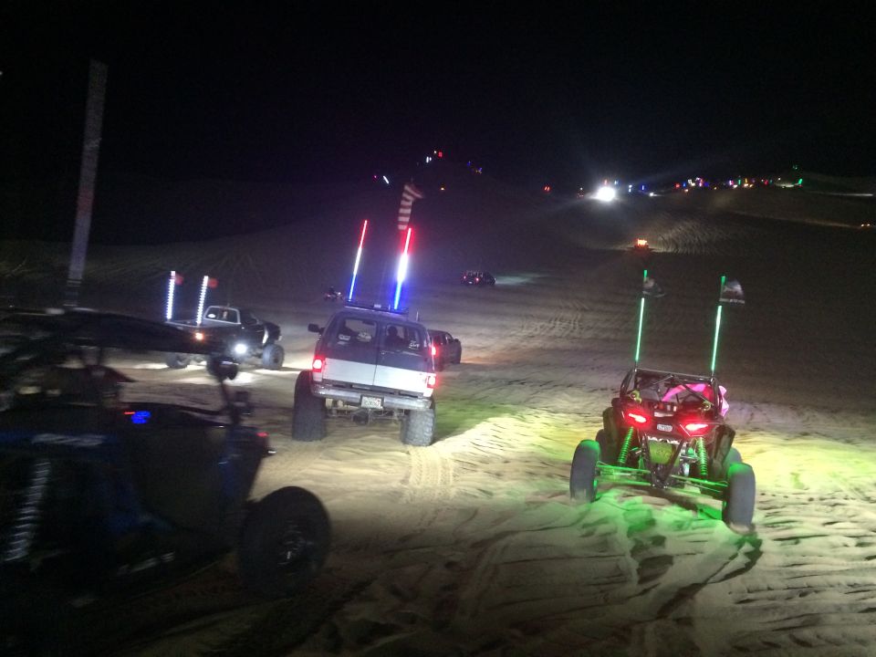 Off-road vehicles with LED light whips driving on sand dunes at night.