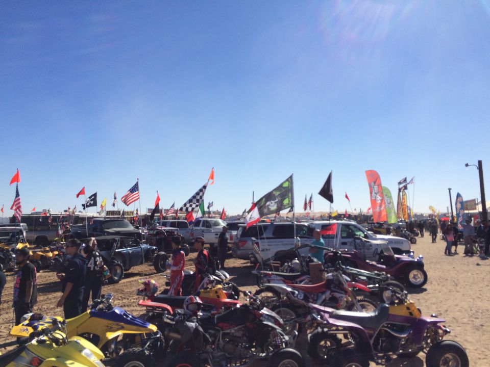 Outdoor event with ATVs, dirt bikes, and vehicles decorated with flags.