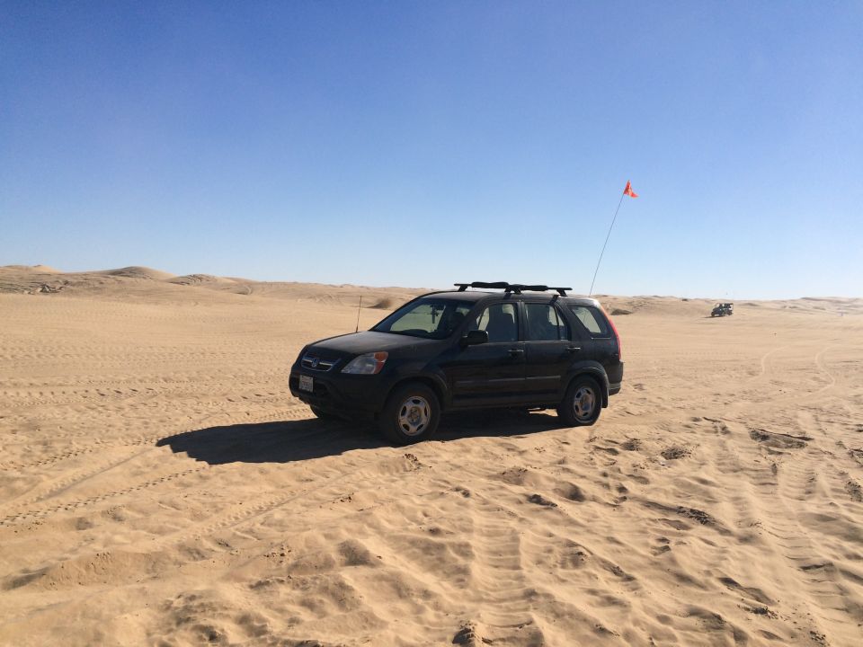 Black Honda CR-V parked on a sand dune with an orange flag.