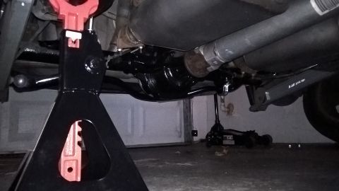 2004 Ford Crown Victoria - The underside of a vehicle is supported by jack stands, with a differential and exhaust system visible. A floor jack is also present on the…