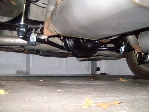 2004 Ford Crown Victoria - The underside of a vehicle shows a black sway bar attached to the differential with silver clamps and bushings. A large exhaust pipe runs p…