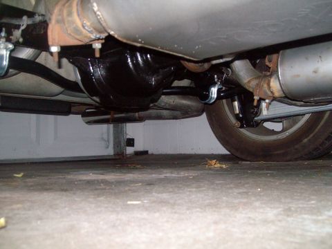 2004 Ford Crown Victoria - The underside of a vehicle is shown, focusing on the rear differential, exhaust system, and a portion of the rear wheel. The differential h…