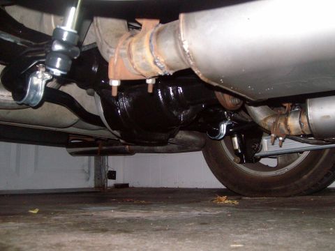 2004 Ford Crown Victoria - The underside of a vehicle showing the rear differential, exhaust system, and a portion of the rear tire. The differential is painted black…