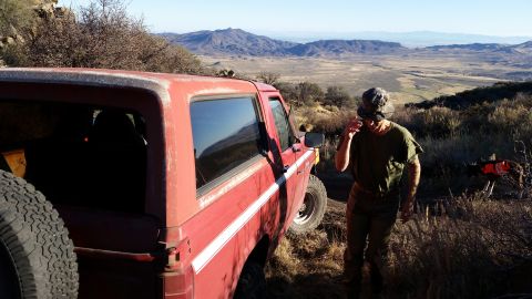 1981 Ford Bronco - A red 1980s Ford Bronco is parked on a dirt road with a man and a dog standing nearby, overlooking a vast valley and distant mountains.