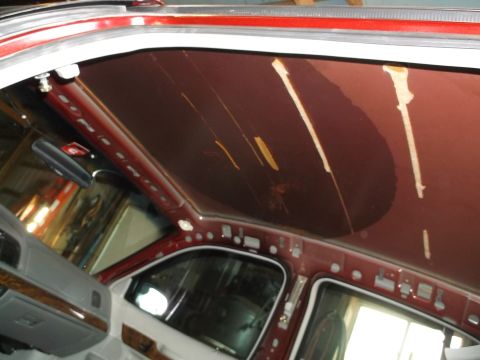 1999 Mercury Grand Marquis - The interior headliner of a red sedan is detached and sagging, revealing the car's roof structure and some water damage.