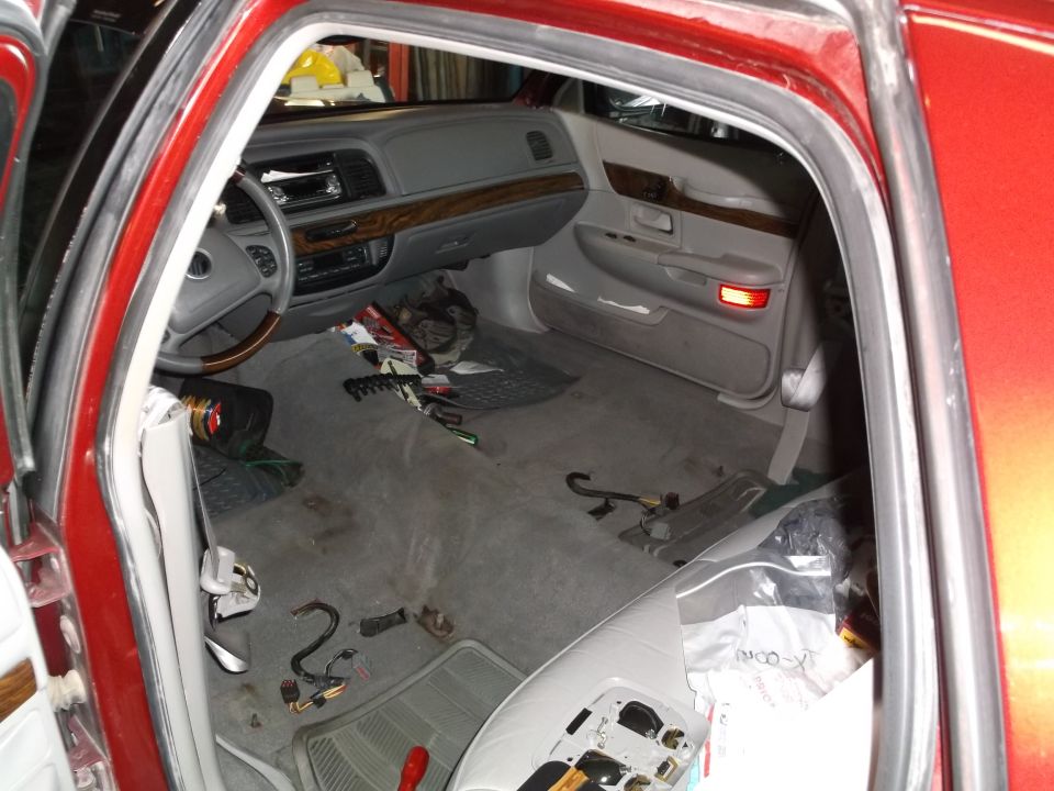 Interior of a red sedan with doors open, showing a cluttered dashboard, steering wheel, and floor with tools and parts.
