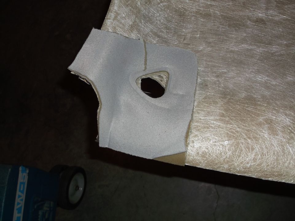 Close-up of a gray fabric piece with a hole on a textured beige surface. Blue object with wheels in corner.