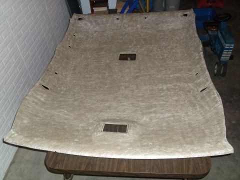 1999 Mercury Grand Marquis - A tan headliner is laid out on a table. There are cutouts for lights and a sunroof.