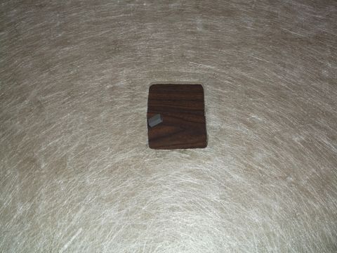 1999 Mercury Grand Marquis - A small, dark brown, square wooden object with a tiny gray rectangular object on top sits on a textured, light-colored surface.