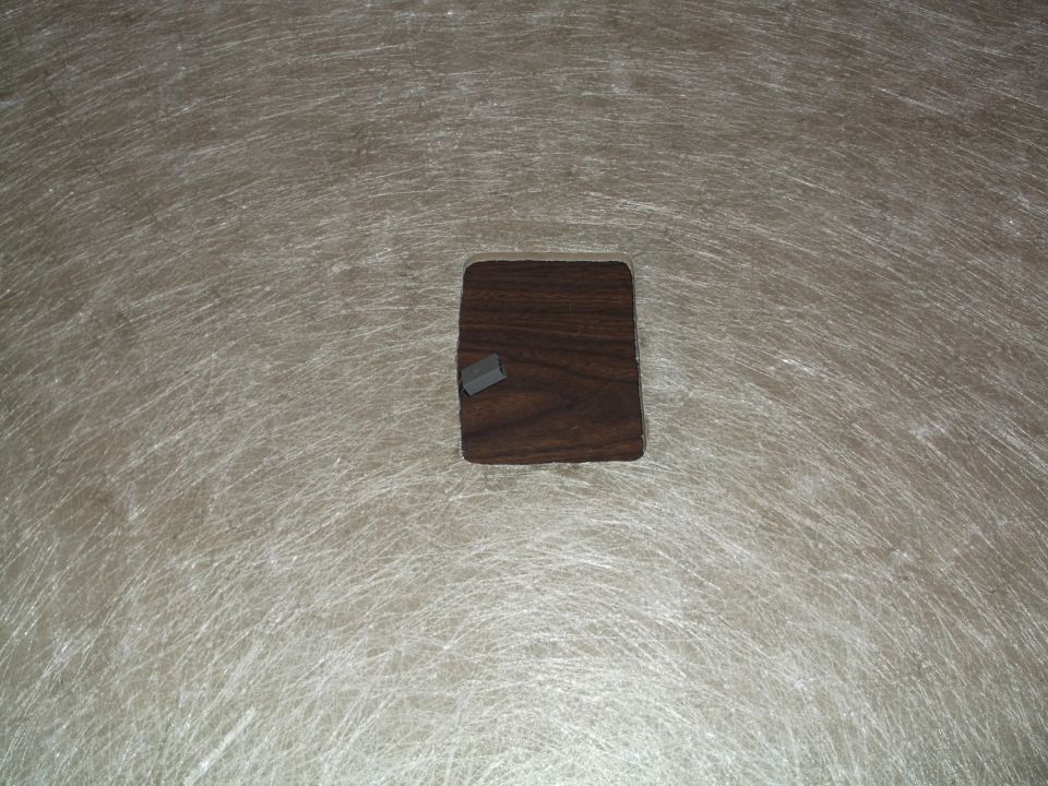 A small wooden square with a gray object on top on a textured surface.