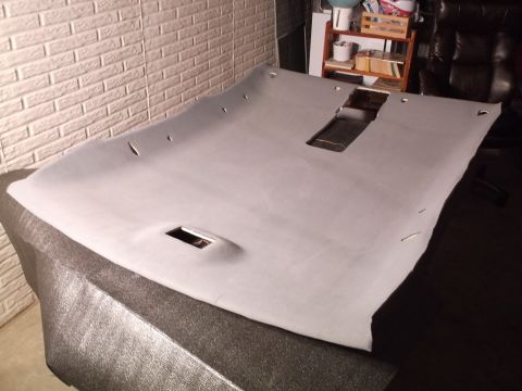 1999 Mercury Grand Marquis - A light gray headliner with cutouts for a sunroof and dome lights is laid out on a textured surface. The headliner appears to be from a car…