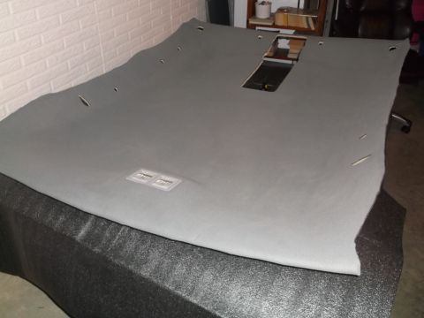 1999 Mercury Grand Marquis - A gray headliner for a 1999 Mercury Grand Marquis is laid out on a black surface. The headliner has cutouts for lights and a sunroof.