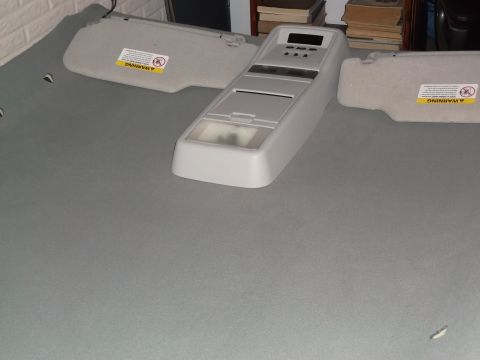 1999 Mercury Grand Marquis - A gray interior overhead console with buttons and a digital display is shown placed on a gray fabric surface, next to two gray sun visors w…