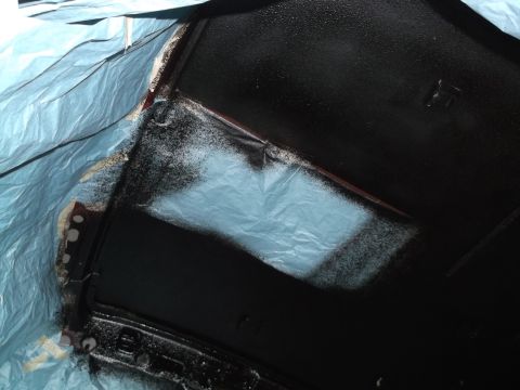 1999 Mercury Grand Marquis - A black painted part is covered with a blue tarp, with some overspray visible on the tarp and the part. The object appears to be a car part…