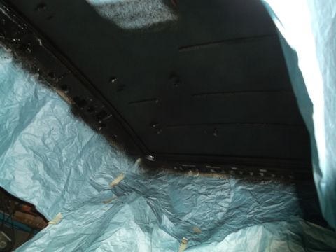 1999 Mercury Grand Marquis - The interior of a vehicle's headliner is being sprayed with a dark coating, with blue plastic sheeting protecting the surrounding area.