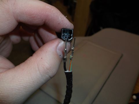 1999 Mercury Grand Marquis - A hand holds a black electrical connector with two wires attached. The wires are green, orange, and black, with metal crimp connectors on t…