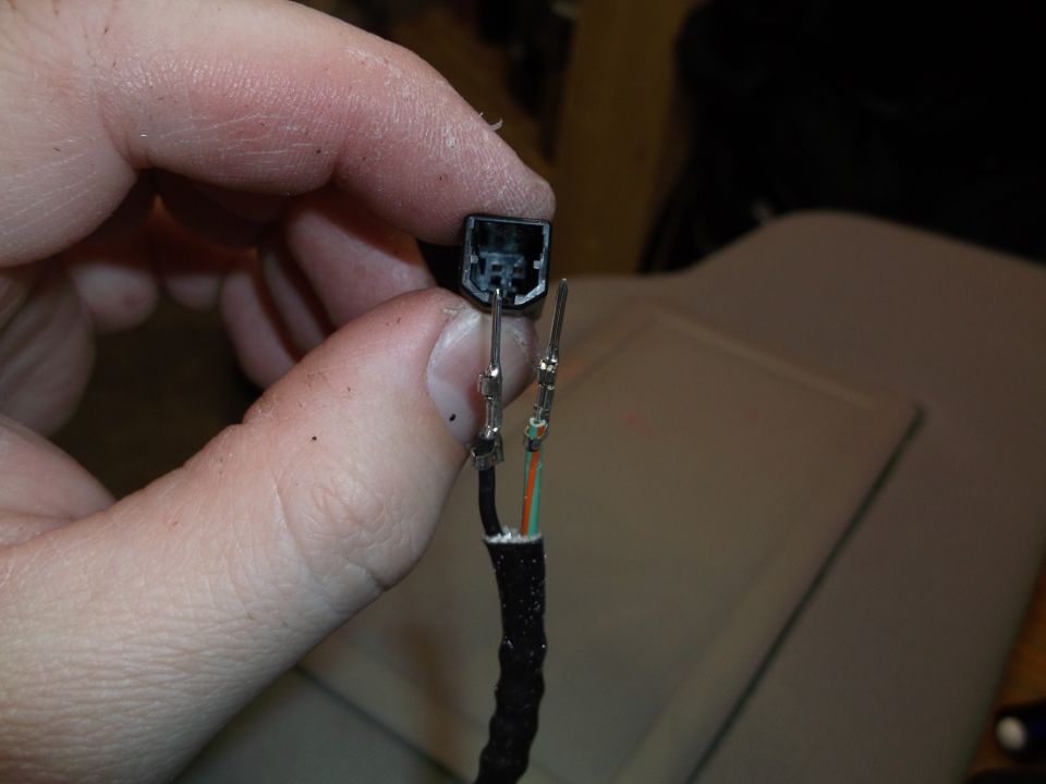 Close-up of a hand holding a black electrical connector with exposed wires.