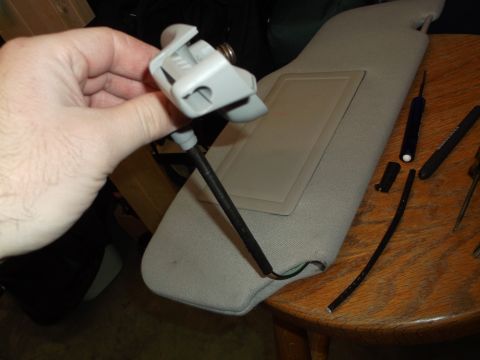 1999 Mercury Grand Marquis - A hand holds a gray plastic part with wires attached, positioned above a gray sun visor on a wooden table. Several tools are scattered arou…