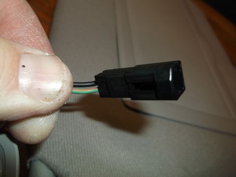 1999 Mercury Grand Marquis - A person's thumb and forefinger are holding a black electrical connector with three wires (black, orange, and green) emerging from it.