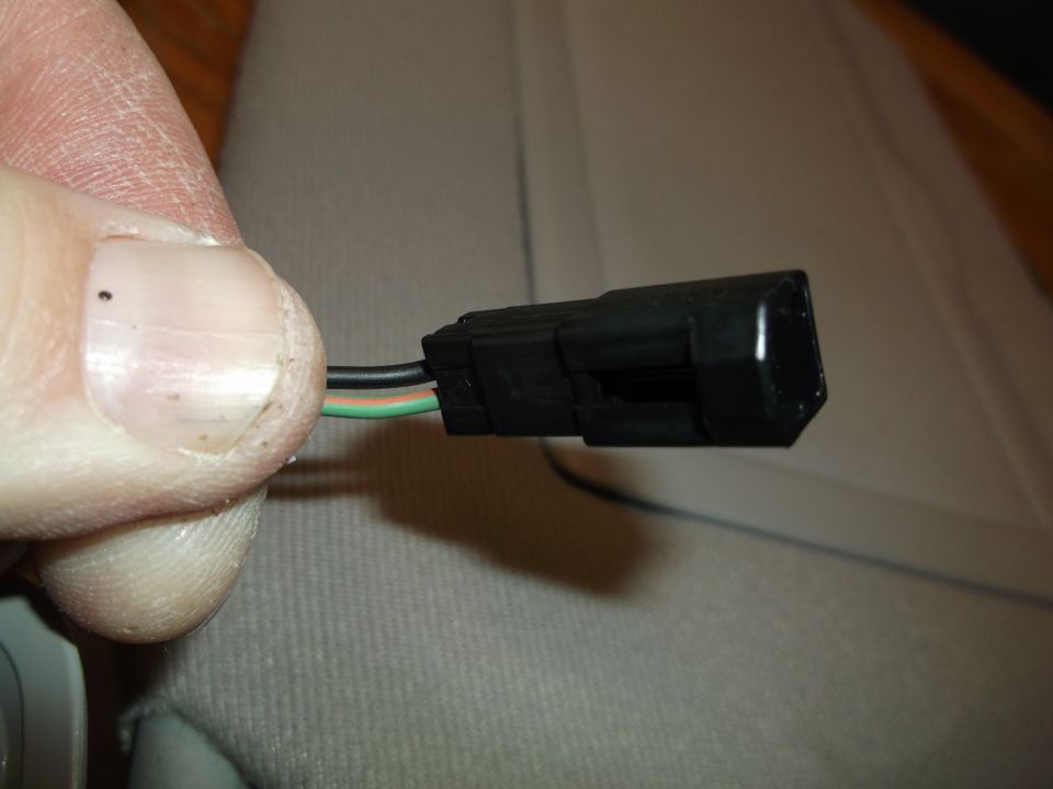 Close-up of a black electrical connector with wires held by a thumb and forefinger.